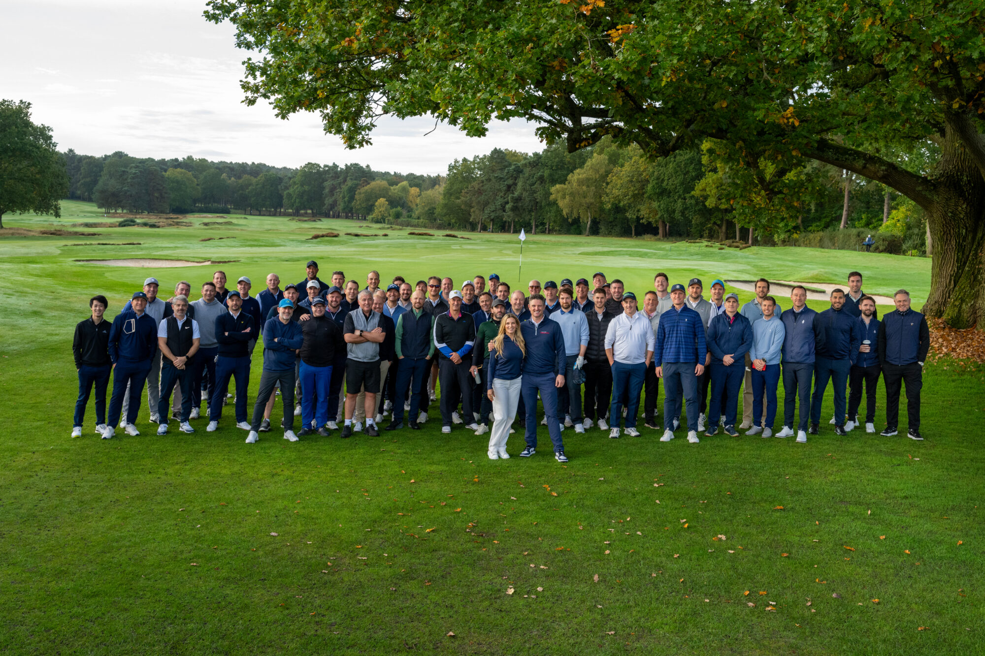 Kate & Justin Rose accompanied by a large group of people in front of a golf green.